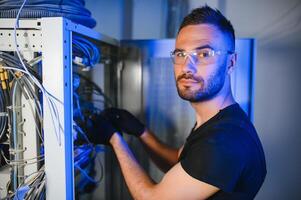 A technician works with server equipment in a data center. A man commutes wires in a server room photo