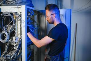 A technician works with server equipment in a data center. A man commutes wires in a server room photo