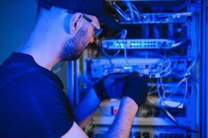 Young man is working with internet equipment and wires in server room photo
