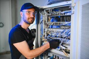 Young man is working with internet equipment and wires in server room photo