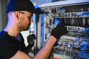 A technician works with server equipment in a data center. A man commutes wires in a server room photo