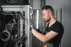 A technician works with server equipment in a data center. A man commutes wires in a server room photo