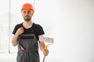 Young cheerful professional painter with paint roller in hands. Repair concept photo