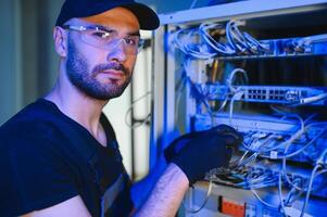 Young man is working with internet equipment and wires in server room photo
