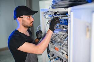 Young man is working with internet equipment and wires in server room photo