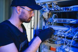 Young man is working with internet equipment and wires in server room photo