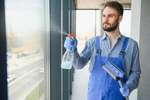 Male professional cleaning service worker in overalls cleans the windows and shop windows of a store with special equipment photo