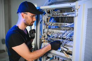Young man is working with internet equipment and wires in server room photo