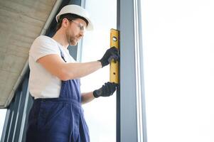 Worker using bubble level after plastic window installation indoors photo