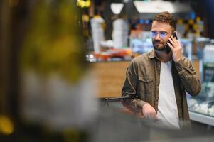 Quick text during shopping. Handsome young man holding mobile phone and smiling while standing in a food store photo