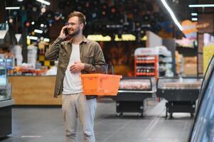 Quick text during shopping. Handsome young man holding mobile phone and smiling while standing in a food store photo