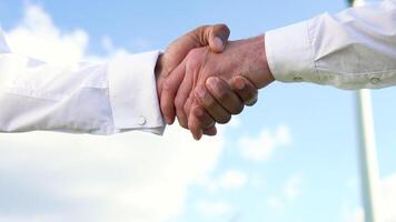 Close up two multiracial man wind turbine engineers working and shaking hands at wind turbine farm on background, renewable energy video