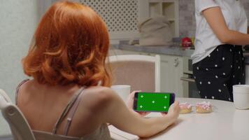 Back view of woman at horizontal phone with green screen not paying attention to her friend talk. video