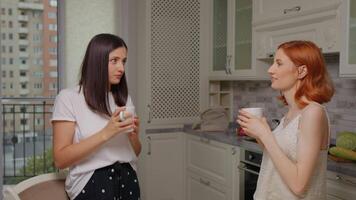 Best friends talking and standing up while drinking coffee together in the kitchen. video