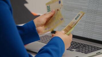 Side view woman that counts money in bills in front of a laptop. video