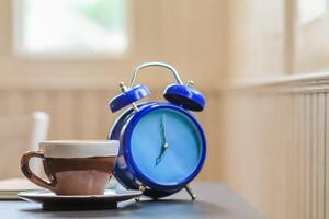 The alarm clock set by the window in the morning beside the coffee cup is used to set the time to remind appointments, is an analog alarm clock that sends alarms by tapping the side bell. photo