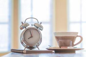Alarm clocks and coffee mugs are placed on a wooden table by the window in the morning to prepare to work at home to help reduce the spread of coronavirus covid-19. The concept of work from home photo