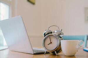 Alarm clocks and coffee mugs are placed on a wooden table by the window in the morning to prepare to work at home to help reduce the spread of coronavirus covid-19. The concept of work from home photo