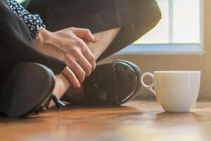 A girl sipping coffee on a wooden floor by the window in the house to see the scenery outside the house and having a coffee break before starting work at home. Continue the work from home concept photo