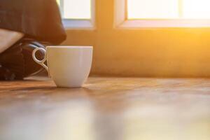 A girl sipping coffee on a wooden floor by the window in the house to see the scenery outside the house and having a coffee break before starting work at home. Continue the work from home concept photo