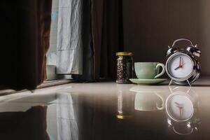 The alarm clock set by the window in the morning beside the coffee cup is used to set the time to remind appointments, is an analog alarm clock that sends alarms by tapping the side bell. photo