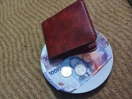 Ceramic cup with wallet and Indonesian rupiah banknotes on yellow carpet background photo