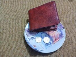 Ceramic cup with wallet and Indonesian rupiah banknotes on yellow carpet background photo