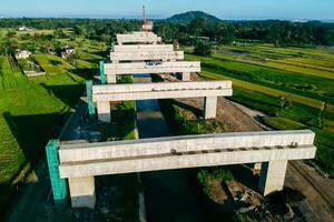 Sleman, Yogyakarta, Indonesia, 2024 - Toll road construction project over the Mataram ditch. A toll bridge is being built over the water flow so as not to displace rice fields and settlements photo