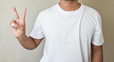 A man dressed white t-shirt keeping forefinger raised while counting two photo
