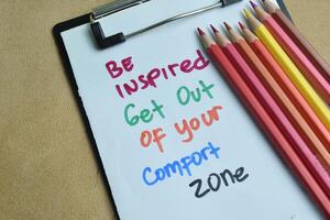 Concept of Be Inspired Get out of your comfort zone write on paperwork isolated on wooden background. photo