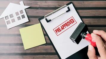 Red Handle Rubber Stamper and Pre-Approved text above paperwork isolated on wooden background photo