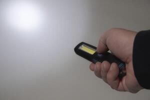 Pocket led flashlight in hand. illuminates gray background. Copy space. Circle of light photo