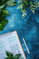 Clipboard with financial data on a blue surface with green plants, copy space photo