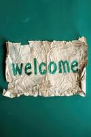 A welcome sign on crumpled paper on green background photo