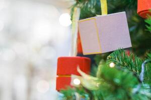 Close-up view of a Christmas tree decoration, in the shape of a red cylinder and purple box with blurred lights in bokeh on a background photo