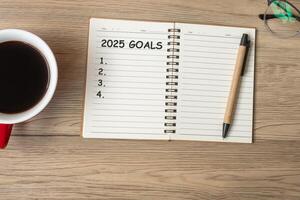 2025 GOAL with notebook, black coffee cup and pen on wood table, Top view and copy space. Happy New Year, Resolution, To do list, Strategy and Plan concept photo
