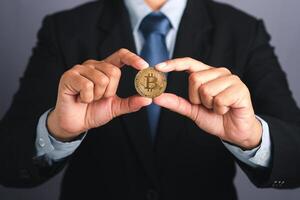 Hand of businessman showing a bitcoin golden coin while standing with a gray background. Close-up photo. Space for text. Virtual cryptocurrency and future money concept photo