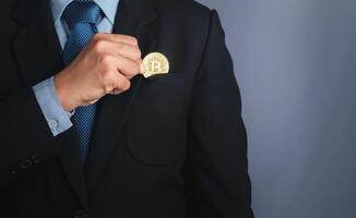 An investor guy holding a bitcoin golden coin put to suit pocket with a gray background. Close-up photo. Space for text. Virtual cryptocurrency and future money concept photo