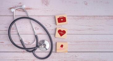 A stethoscope and wooden blocks with icons of health laid on wooden table. Close-up photo. Top view. Flat lay with Space for text. Healthcare and medicine with media icons concept photo