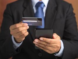 Businessman using a smartphone with a credit card while standing in the studio with a vintage background. Close-up photo. Space for text. Communication, technology, e-commerce, and business concept photo