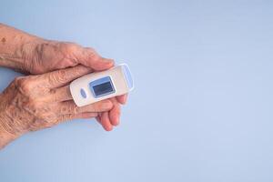 Senior woman finger with a pulse oximeter for testing oxygen levels on a blue background. Close-up photo. Measurement of oxygen level in the blood. Healthcare concept photo