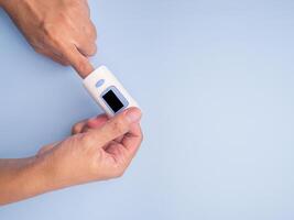 Pulse oximeter on the index finger on a light blue background. Measurement of blood oxygen and pulse. Lung disease. Close-up photo. Space for text. Healthcare concept photo