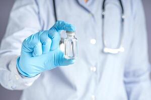 Doctor showing a vaccine bottle while standing with a gray background. Vaccine for immunization, and treatment from virus infection. Concept of medical and the fight against the virus photo