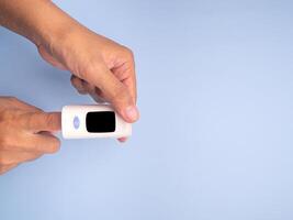 Pulse oximeter on the index finger on a light blue background. Measurement of blood oxygen and pulse. Lung disease. Close-up photo. Space for text. Healthcare concept photo