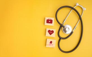 Stethoscope and wooden blocks with icons of health isolated on a yellow background. Close-up photo. Top view. Flat lay with Space for text. Healthcare and medicine with media icons concept photo