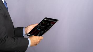 Side view of a businessman holding and reading business graphs and stock charts on a digital tablet. Stock market investments funds and digital assets. Business finance and investment concept photo
