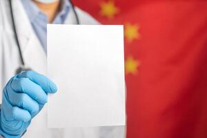 Doctor hand holding a white paper while standing with the China flag background. Space for text. Medical and information concept photo