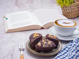 Pieces of fresh brownies on a plate with a book and a white coffee cup. Side view. Delicious chocolate pie. Dessert, beverage, and relaxation concept photo
