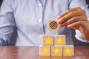 Close-up of hand holding a wooden block with the five-star and target symbol. Concept of business, feedback, and service serving concept photo
