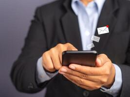 Businessman using a smartphone with an email icon while standing with a gray background. Space for text. Communication and technology concept photo